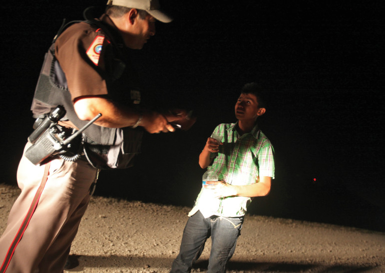 A Hidalgo county constable gives water to a boy crossing the border with two other immigrants as they wait for the U.S. Border Patrol to arrive in August near Granjeno.