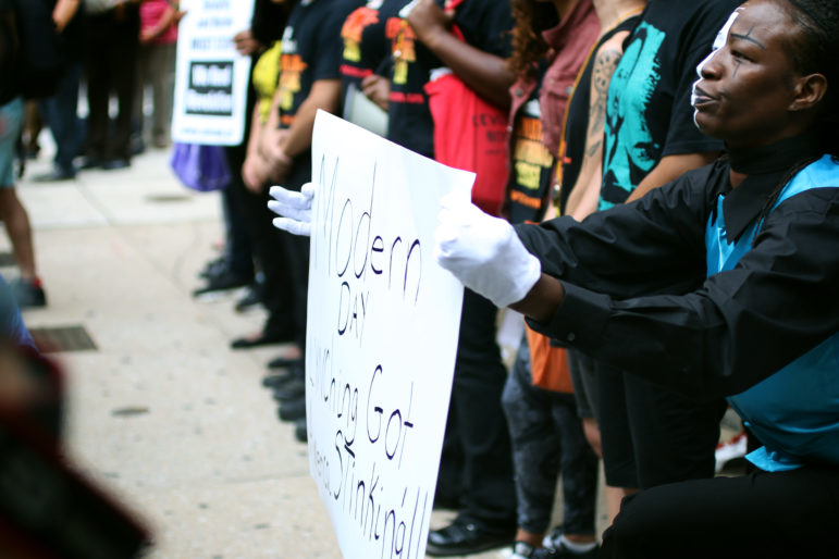 A mime artist holds a sign reading “Modern day lynching got America stinking” during a protest following the acquittal from murder charges of one of the police officers involved in the death of Baltimore resident Freddie Gray.