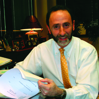 Shay Bilchik (headshot), smiling man with gray beard and mustache wearing white shirt, yellow polka-dotted tie