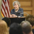 (headshot), Jane Guttman, smiling woman with short, curly gray hair at lectern