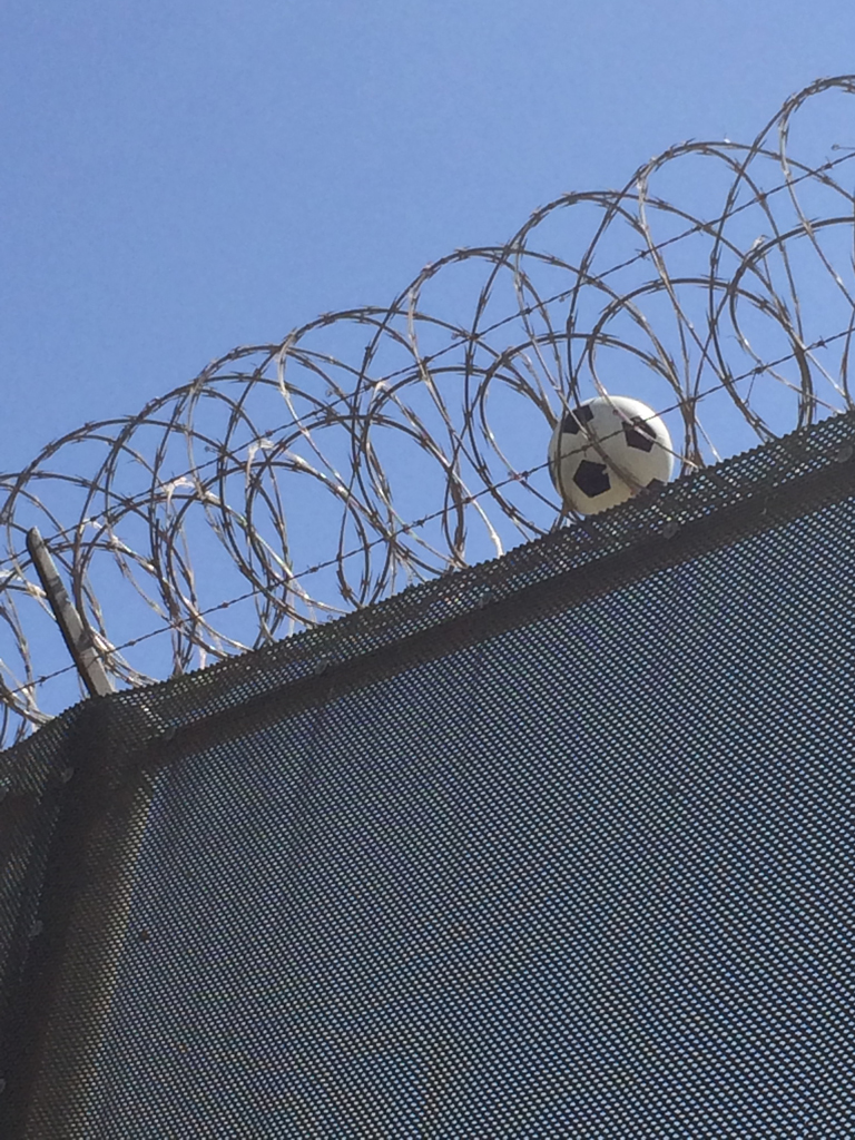 alt text: California: Soccer ball caught in barbed wall on top of wall.