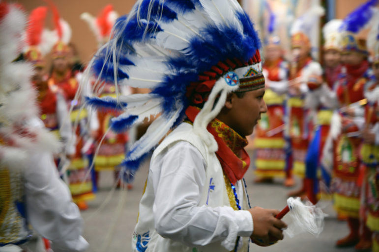 Boy in white costume with full headdress of blue and white feathers.