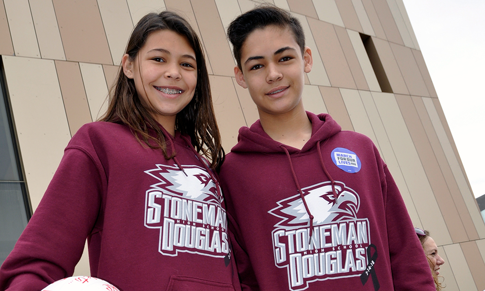 Marjory Stoneman Douglas High School student Trey Patton and his sister Evelyn at March for Our Lives. She is carrying a red and white basketball; he a red and white shopping bag. Both are wearing maroon Stoneman Douglas sweatshirts.