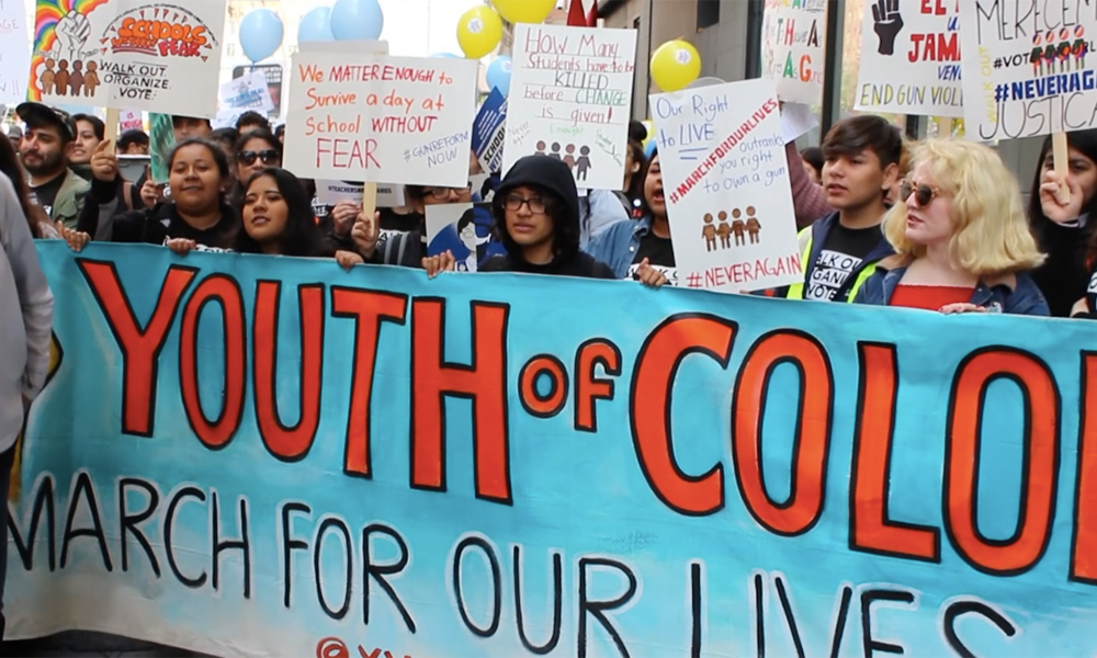 March for Our Lives: Young people carry a blue banner labelled “Youth of Color, March for Our Lives.”