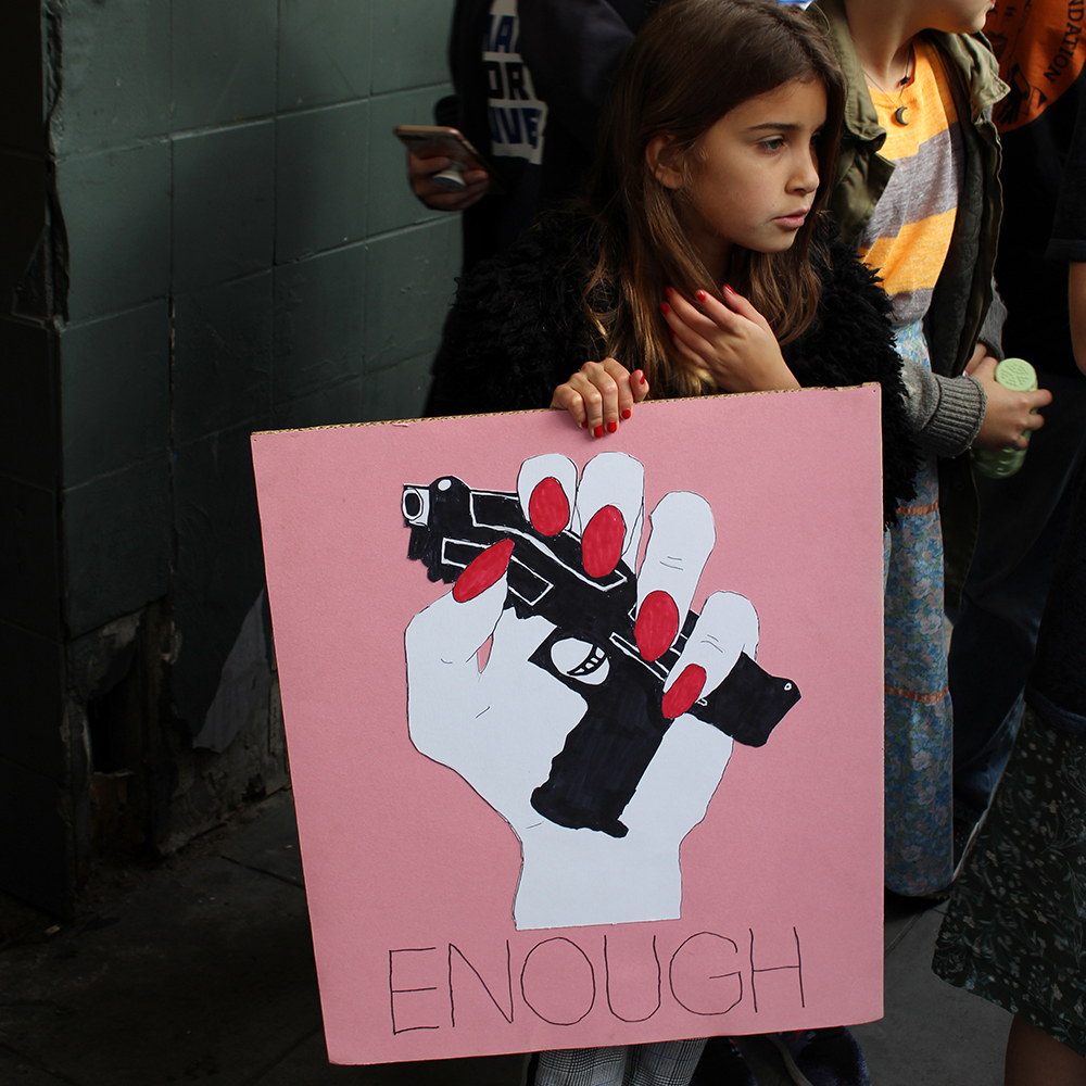 March for Our Lives: A little girl in nail polish looks somber as she holds her sign.