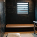 3 black walls, dark table on right, wooden bench attached to back wall.