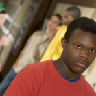 DMC: Serious-looking African-American teen in red T-shirt stands alone near locker, 3 other teens are in background.