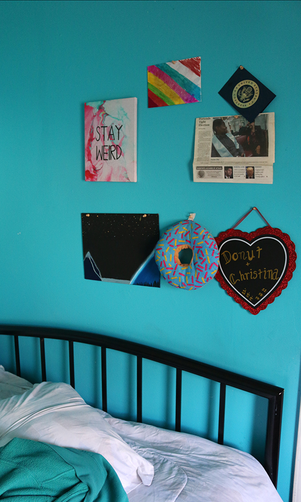Homelessness: Colorful hangings on blue wall above bed include sign that says Stay Weird, a newspaper article and a heart that says Donut + Christina.