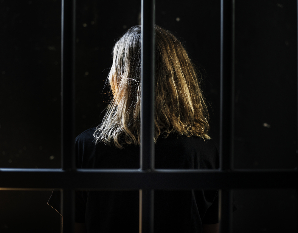 Woman seen from back, dressed in black, behind bars, with only hair spotlighted.