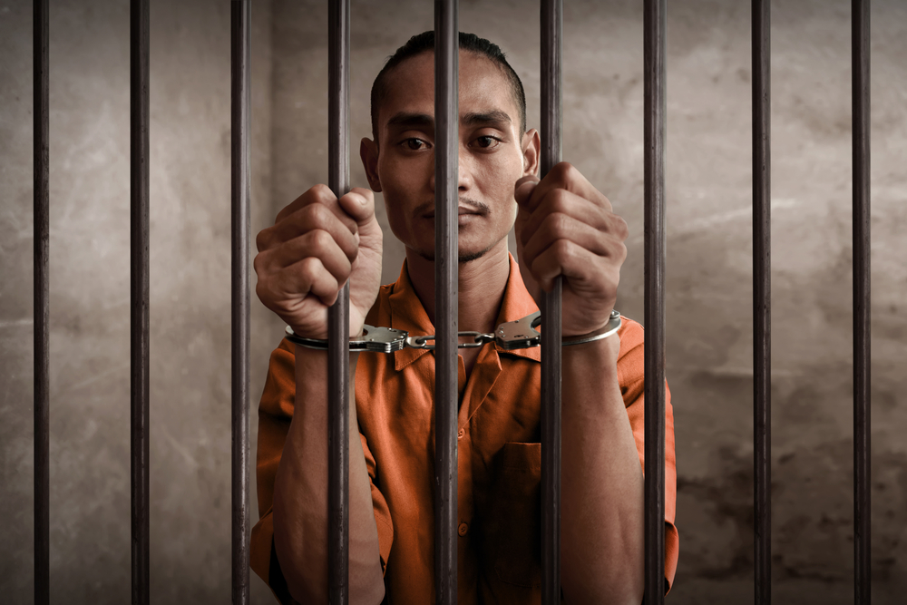 JLWOP: Young man in orange jumpsuit behind bars.