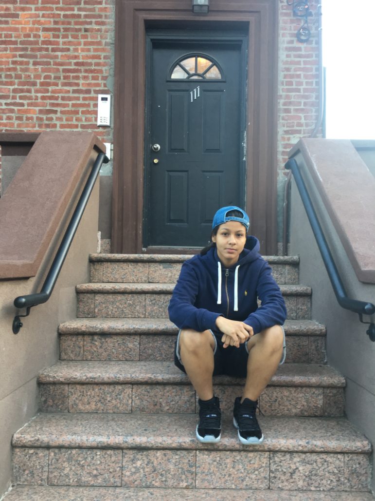 Civil rights: Young woman in navy blue hoodie, shorts, black sneakers and blue ball cap worn backwards sits on steps of building.