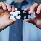 Racial bias: A businessman in a suit holding a white puzzle piece and a black unites them.