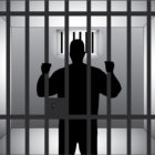 Solitary confinement: silhouette of single man behind bars holding onto them.