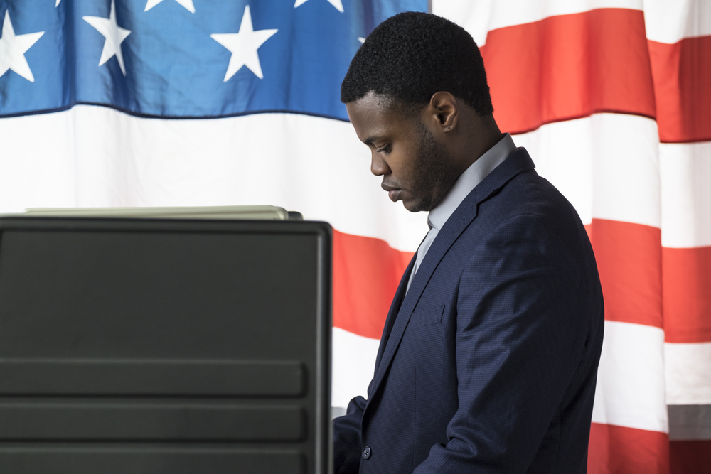 A young man of color in a voting booth, side view.