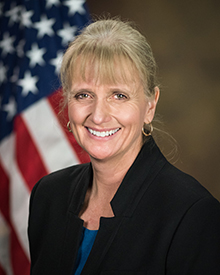 DMC: Caren Harp (headshot), Administrator of the Office of Juvenile Justice and Delinquency Prevention, smiling blond woman in black jacket, blue top.
