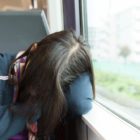 California: Young person sleeping on train or bus beside window with hair over face