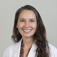 health gap: Smiling woman with long brown hair, earrings, wearing white doctor’s coat