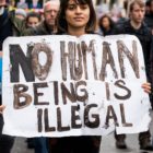 immigrants: Woman in crowd of protesters holds sign that says No human being is illegal.