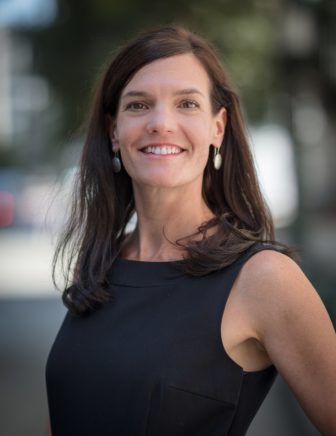 racial and ethnic disparities: Laura Ridolfi (headshot), Director of Policy of W. Haywood Burns Institute, smiling woman with long brown hair, earrings, black dress