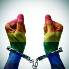 LGBTQ: closeup of the handcuffed hands of a young man patterned as the gay pride flag