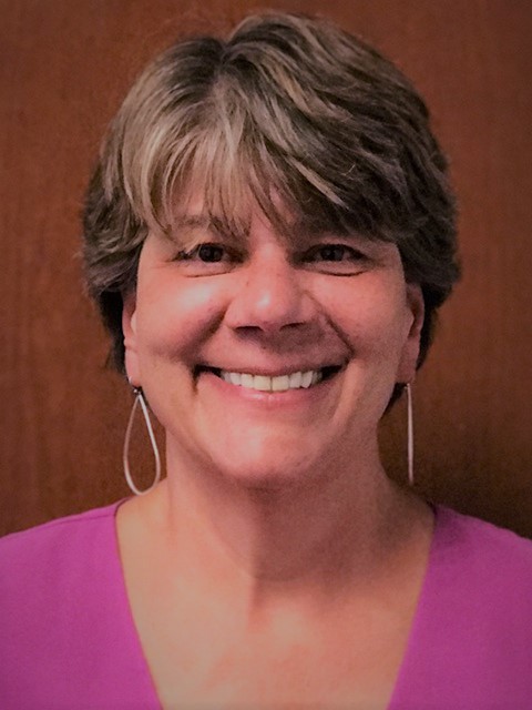 evidence-based practice: Meg Williams (headshot), manages Office of Adult and Juvenile Justice Assistance at Colorado Division of Criminal Justice, smiling woman with short brown hair, long earrings, pink top