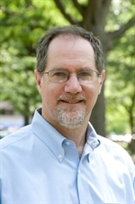 community alternatives: Marc Schindler (headshot), executive director Justice Policy Institute, smiling gray-haired man with mustache, beard, glasses wearing light blue shirt
