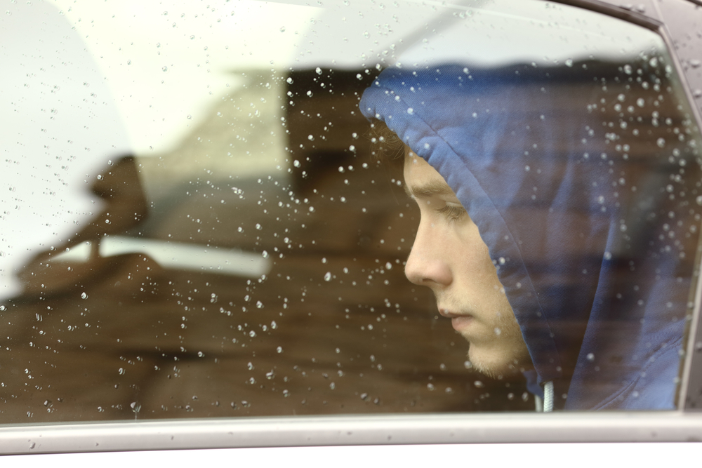community-based programs: Sad teenager boy worried looking through window