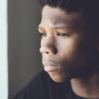 mental health treatment: Faded retro portrait of a worried young African boy staring off to the side with a sad expression and frown in a close-up side view