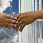 Woman’s hand touches hand of husband to prison with a cloud sky background. Tags: freedom, love, sacrifice