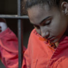lifers: Young woman looking sad holding onto the prison bars