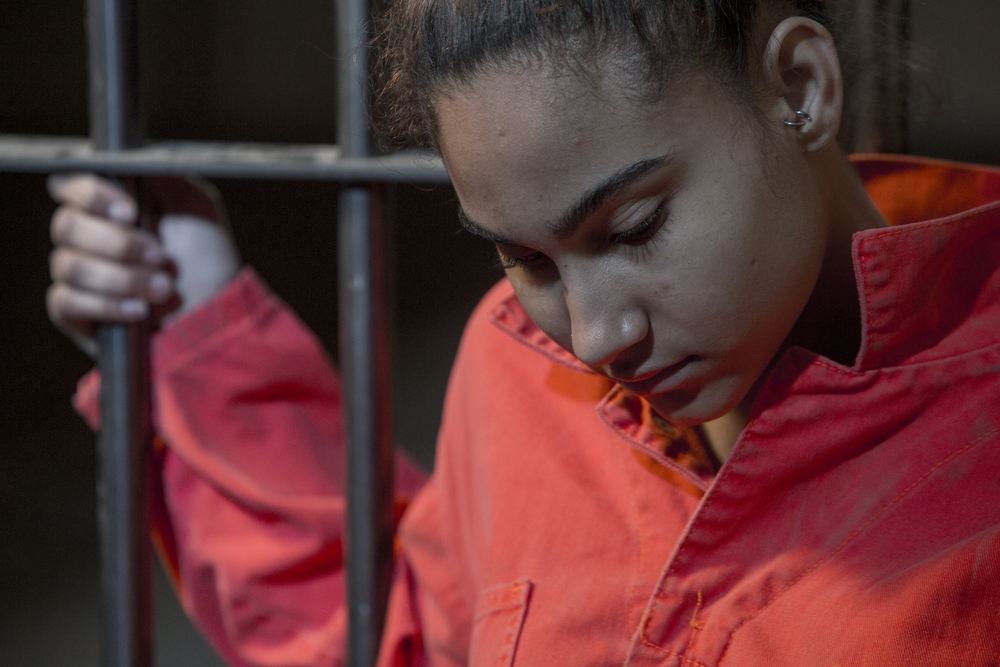 lifers: Young woman looking sad holding onto the prison bars