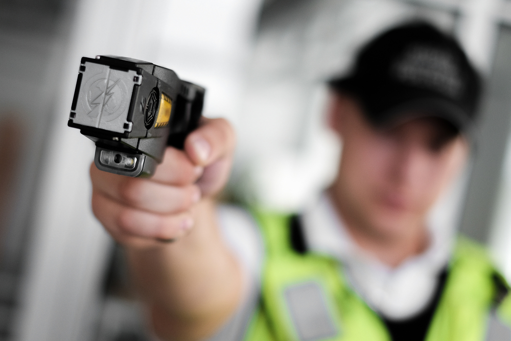 Tasers: Closeup view of a loaded stun gun in a hand of a young man wearing high visibility vest
