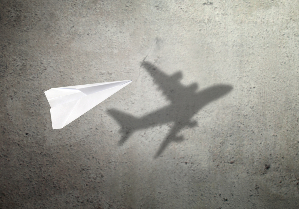 post-traumatic growth: Paper plane in mid flight with shadow of a real plane