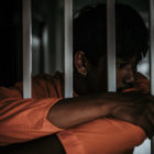 TAG: Youth in orange uniform folds arms around bars.