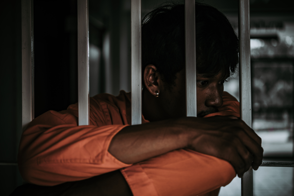 TAG: Youth in orange uniform folds arms around bars.