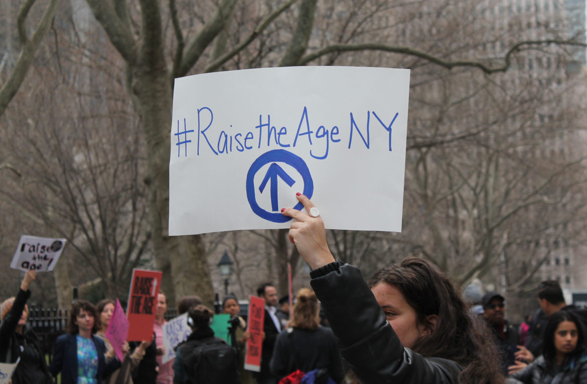 raise the age: Protester holds sign that says raise the age NY