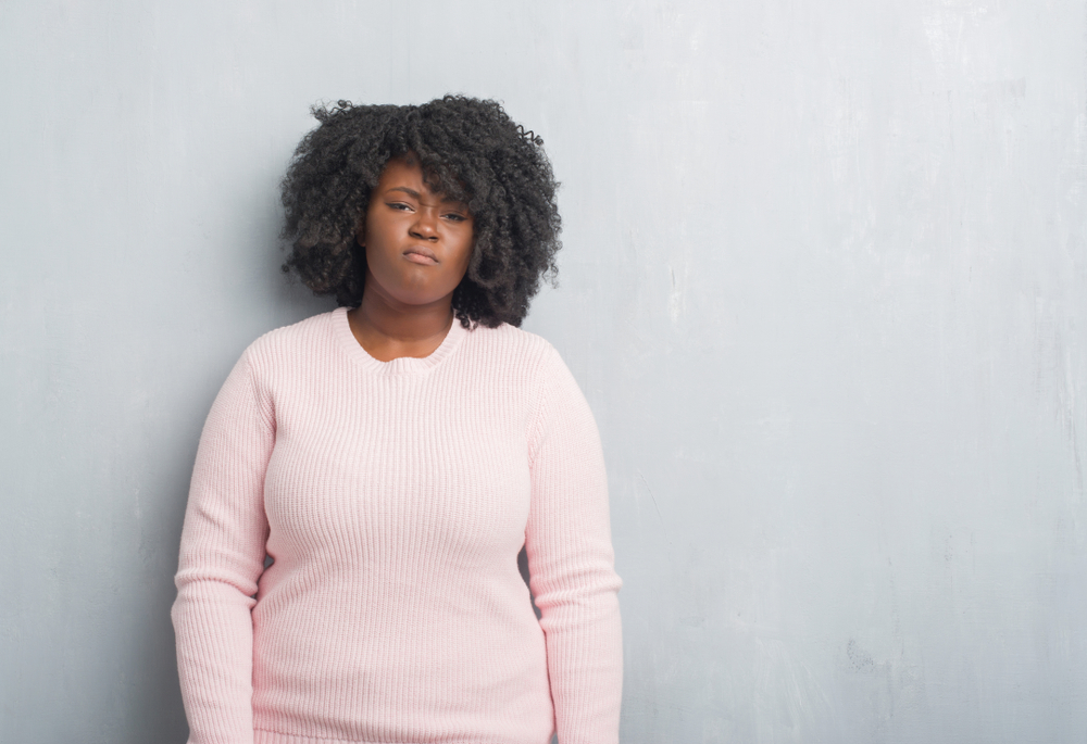 trauma: Young african american plus size woman over grey wall wearing winter sweater skeptic and nervous, frowning upset