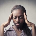 racial and ethnic disparities: African-American young woman with hands to head, looking in pain