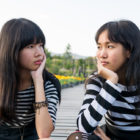 friendship: Two teen girls, hands on chins, elbows on knees, stare at each other.