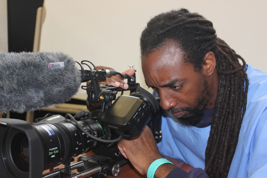 San Quentin: Man in light blue with long dreads leans over camera.