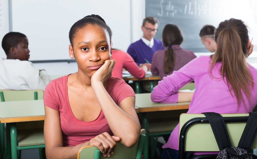 dual system youth: lonely young woman of color sitting away from classmates and feeling depressed