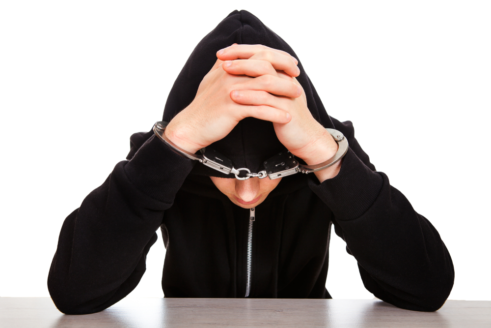 Young man in handcuffs wearing blue hoodie.