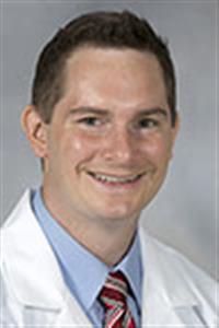 trauma: Smiling man with short dark hair, white doctor’s jacket over light blue shirt, striped tie.