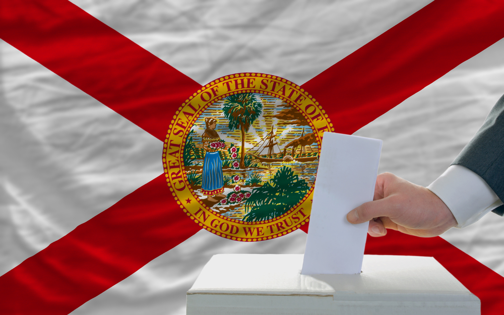 Florida legislature: man putting ballot in a box during elections in front of flag american state of florida