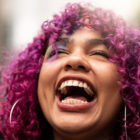 girls: Young woman with curly pink hair throws back head and laughs.