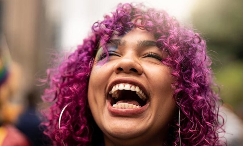 girls: Young woman with curly pink hair throws back head and laughs.