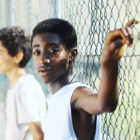 New York City: Young boys of color leaning up against a chain link fence