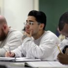 prison education: Men in white sweatshirts sitting at table take notes.