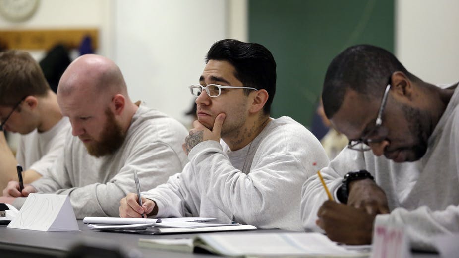 prison education: Men in white sweatshirts sitting at table take notes.