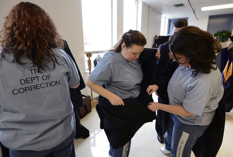 prison education: Women in short-sleeved blue tops with Dept of Correction on back pull on black gowns.